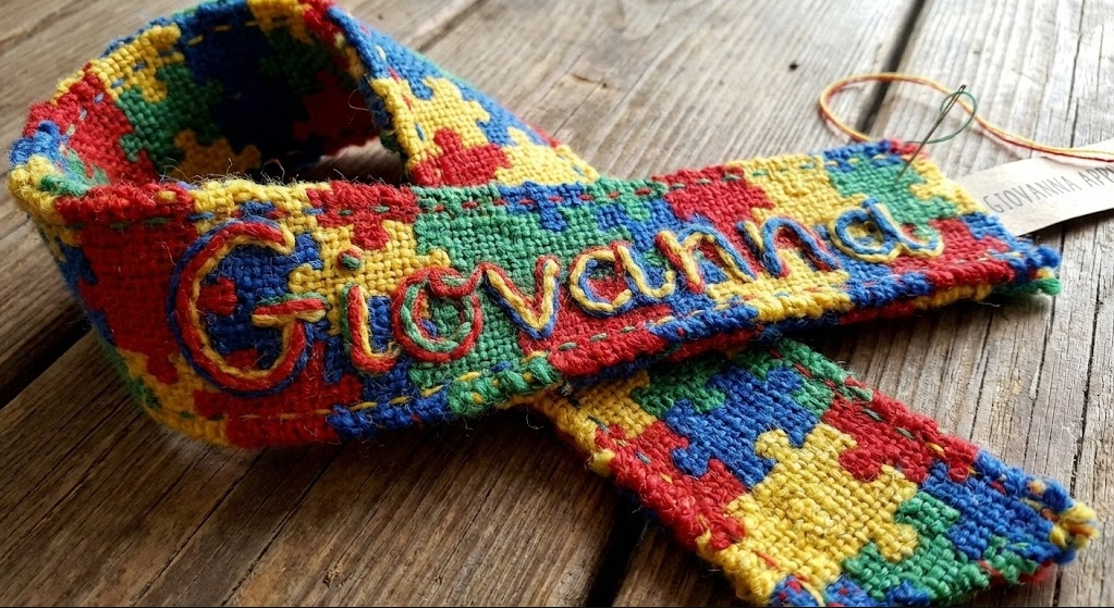 A hand-woven Giovanna ribbon in autism-awareness puzzle colors, resting on weathered wood